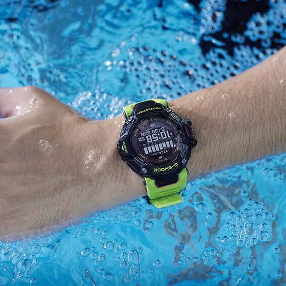 Close-up van een hand in het water, om de pols: het waterdichte GBD-H2000-1A9 sporthorloge