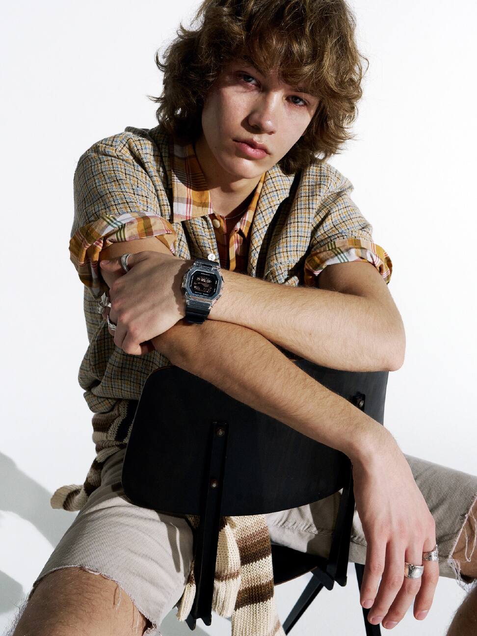Um jovem que usa um G-SHOCK metálico, posando com os braços apoiados numa cadeira.