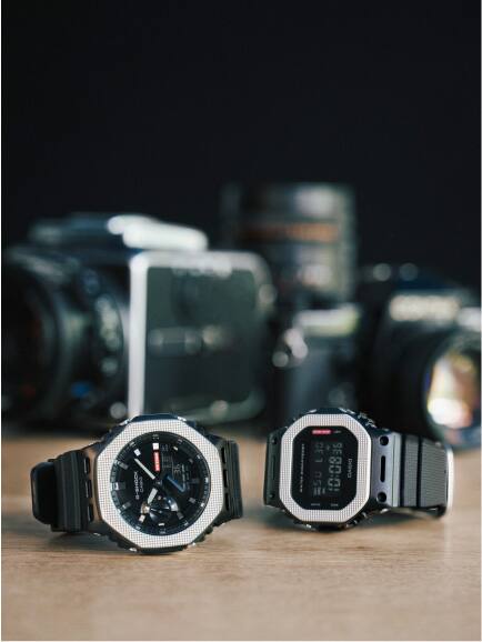 Dois modelos G-Shock com uma luneta prateada e uma bracelete preta apresentados na superfície.