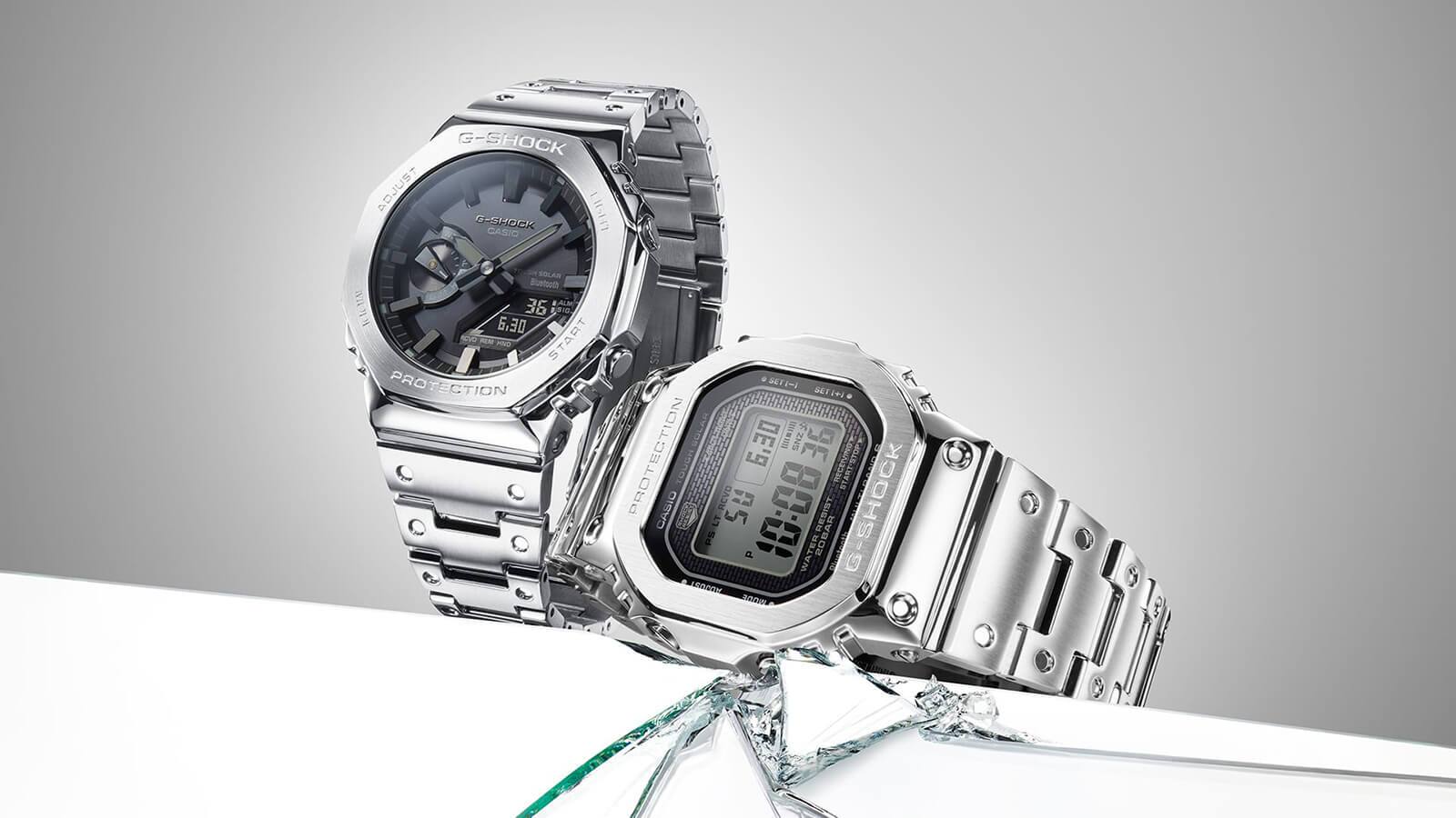 Dois relógios Casio G-Shock prateados em aço inoxidável com um mostrador preto, um relógio híbrido e um relógio digital