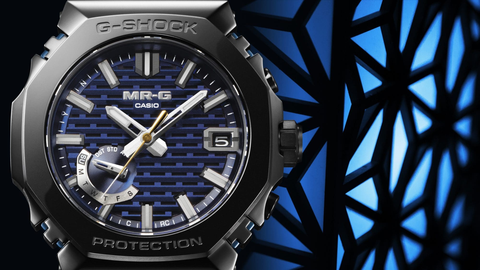 Close-up do mostrador azul do relógio Casio MRG-B2100R-2A preto totalmente em metal, com padrões geométricos em sombra