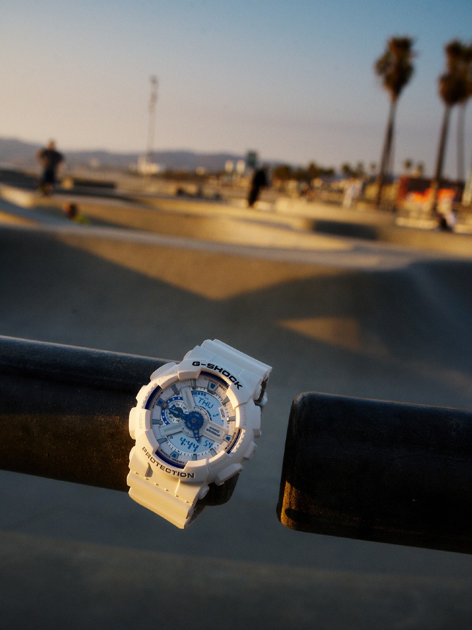 Bir kaykay parkı korkuluğuna asılmış beyaz bir G-SHOCK.