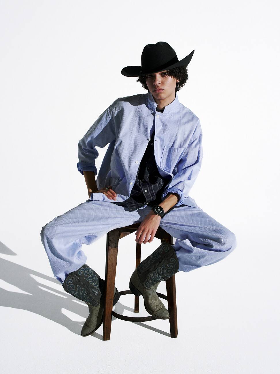 一個人戴著黑色 G-SHOCK 和牛仔帽，穿著靴子坐著拍照。